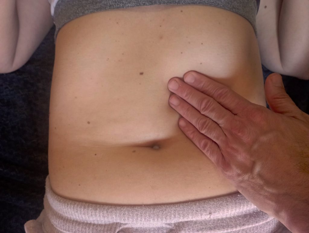 Manos de un terapeuta realizando un drenaje linfático manual en el abdomen de una mujer.